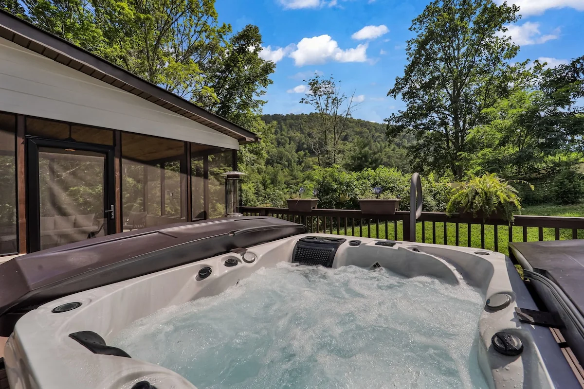 Bubbling deck hot tub looking toward forest and blue sky beside screened porch.
