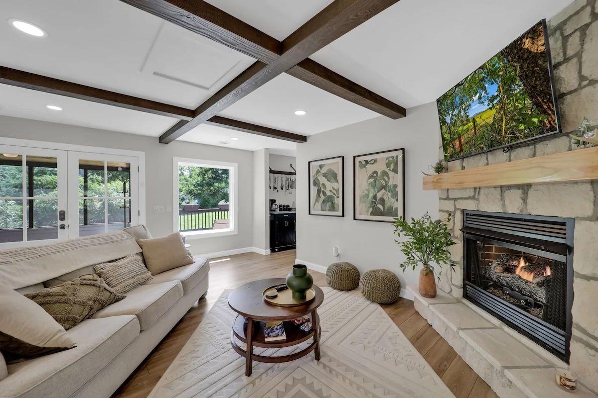 Cottage living room with a sofa, wood ceiling beams, large windows, and a gas fireplace