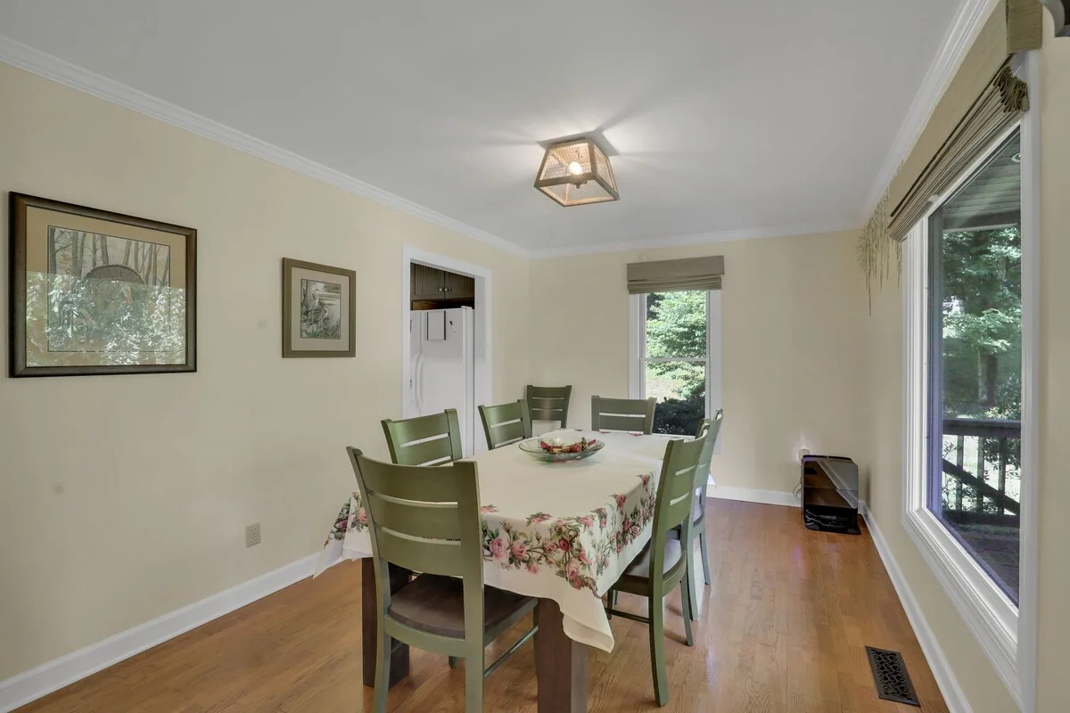 Dedicated dining room with rectangular table, green chairs, large windows, and doorway to deck.