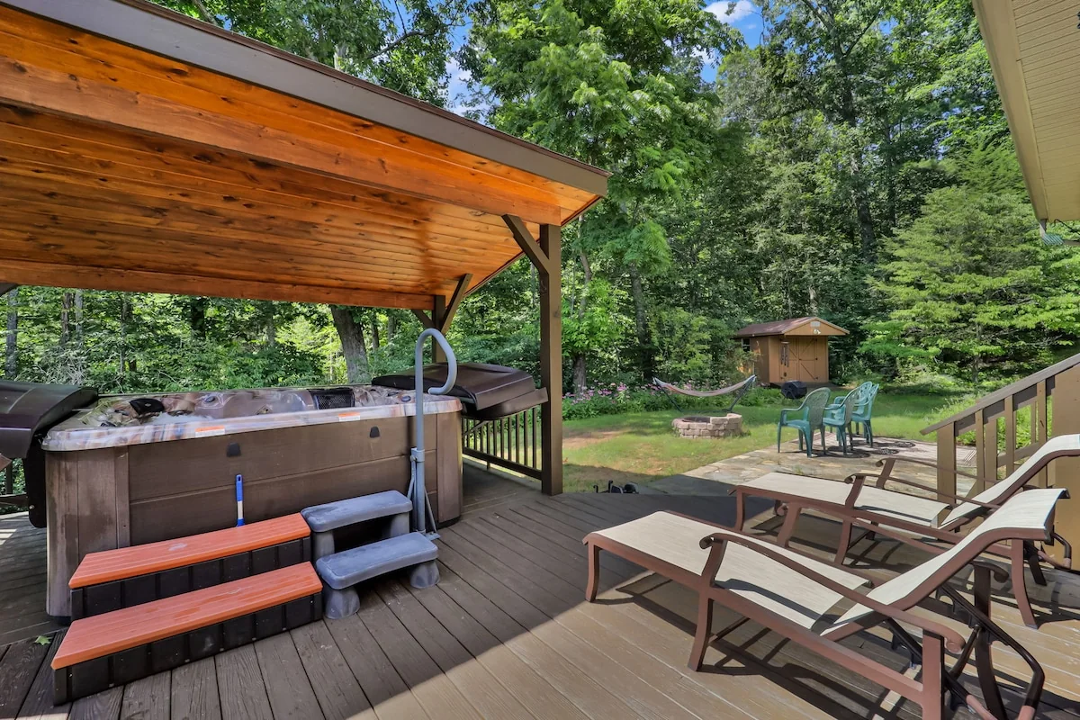 Large covered deck hot tub and lounge chairs with a view across the wooded garden.